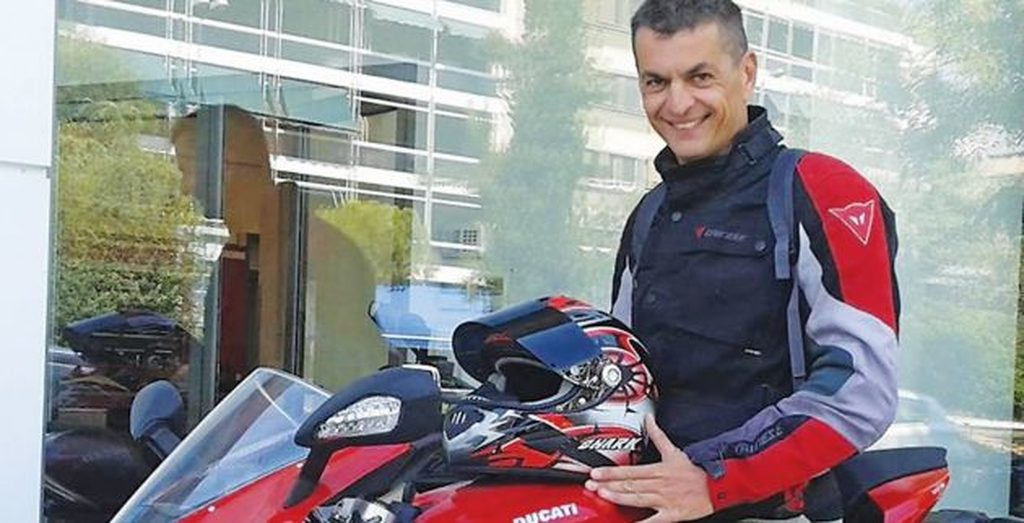 Ο Γιώργος Χρανιώτης με στολή μοτοσικλετιστή δίπλα σε κόκκινη μηχανή Ducati.