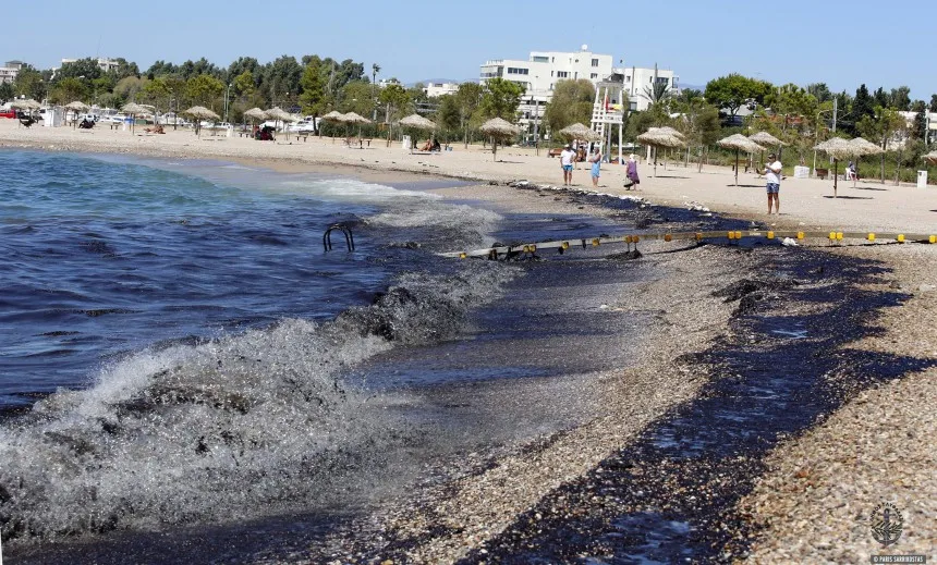 Πετρελαιοκηλίδα σε παραλία της Γλυφάδας με μαύρα κύματα και ρύπανση στην ακτή.
