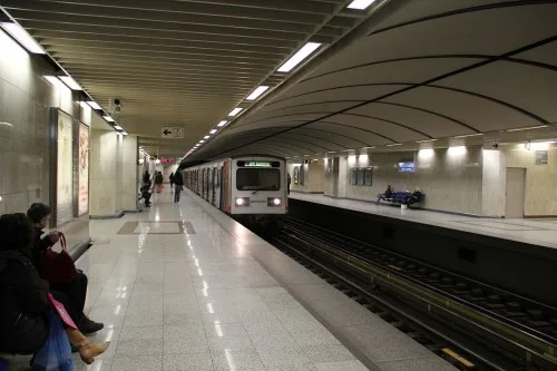 Συρμός του μετρό φτάνει σε αποβάθρα σταθμού με επιβάτες να περιμένουν.