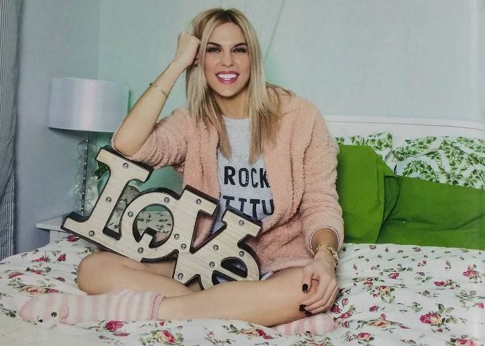 Ξανθιά γυναίκα κάθεται σε κρεβάτι κρατώντας διακοσμητική επιγραφή LOVE.