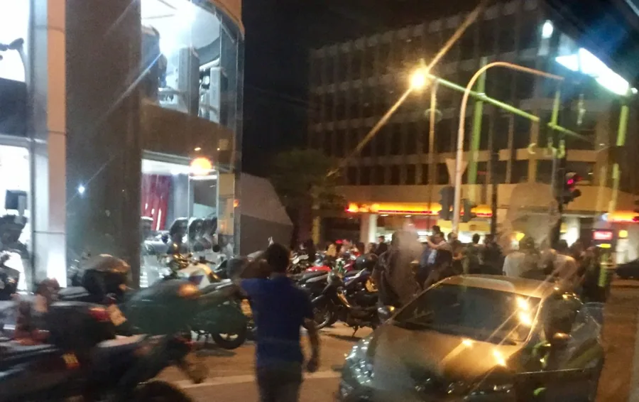 Πλήθος κόσμου και μηχανές έξω από γυμναστήριο το βράδυ.