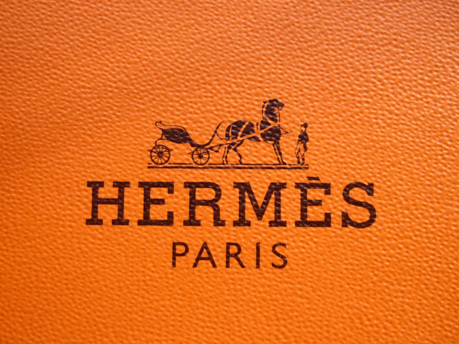 Το λογότυπο του οίκου Hermès Paris σε πορτοκαλί δερμάτινη επιφάνεια.