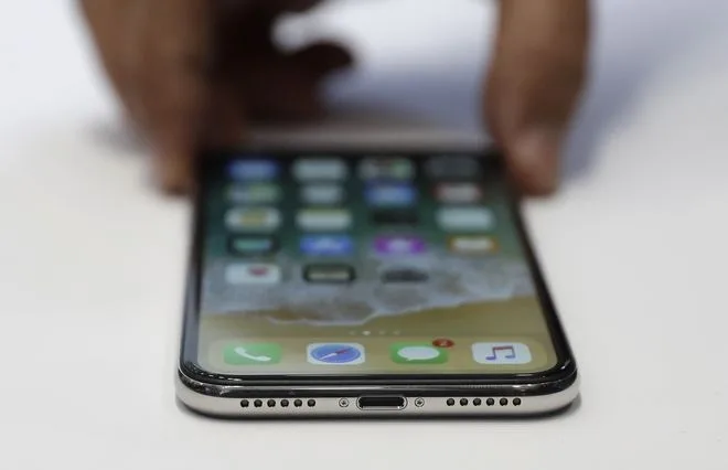 Κοντινό πλάνο ενός iPhone X σε λευκή επιφάνεια με τα χέρια ενός ατόμου να το κρατούν.