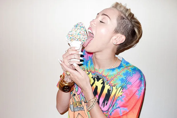Η Miley Cyrus με κοντό ξανθό μαλλί τρώει παγωτό χωνάκι με πολύχρωμη τρούφα.