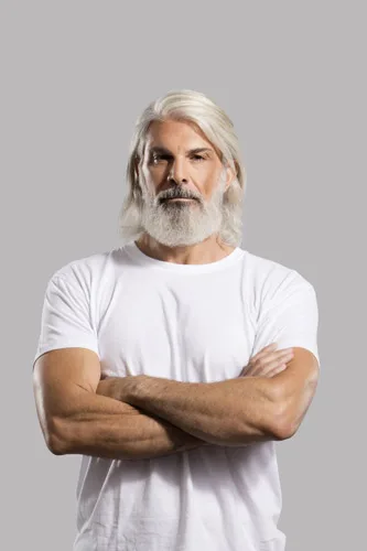Άνδρας με μακριά λευκά μαλλιά και γενειάδα, φορώντας λευκό t-shirt και έχοντας σταυρωμένα τα χέρια.