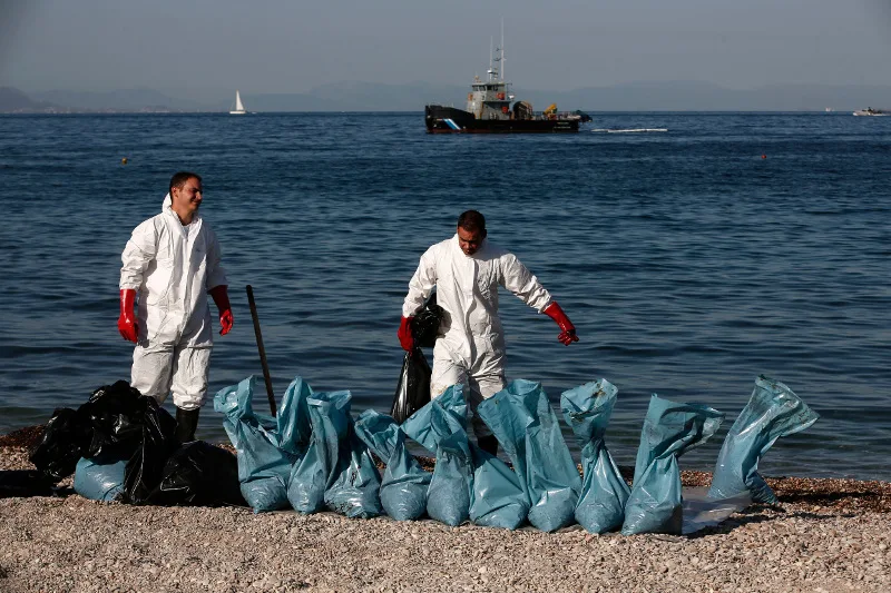 Προσωπικό του Λιμενικού Σώματος καθαρίζει παραλία στη Γλυφάδα από την πετρελαιοκηλίδα του βυθισμένου δεξαμενόπλοιου.