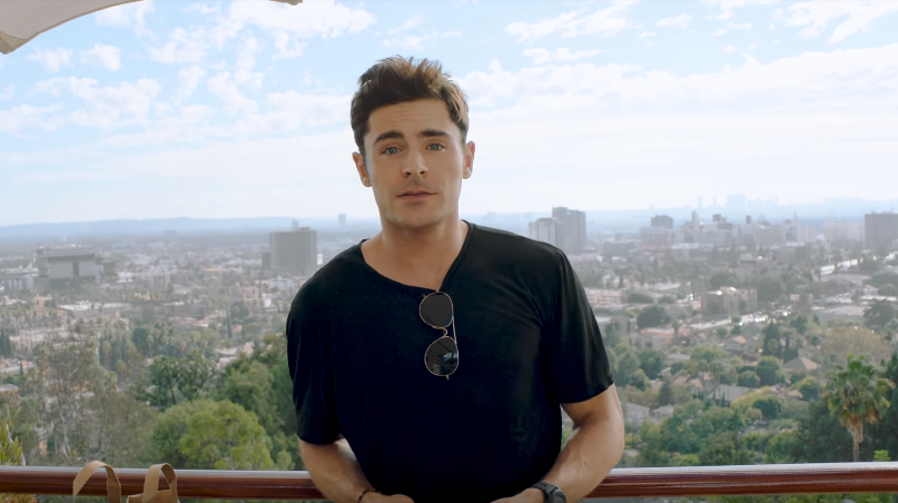 Ο Zac Efron σε εξωτερικό χώρο με θέα την πόλη.