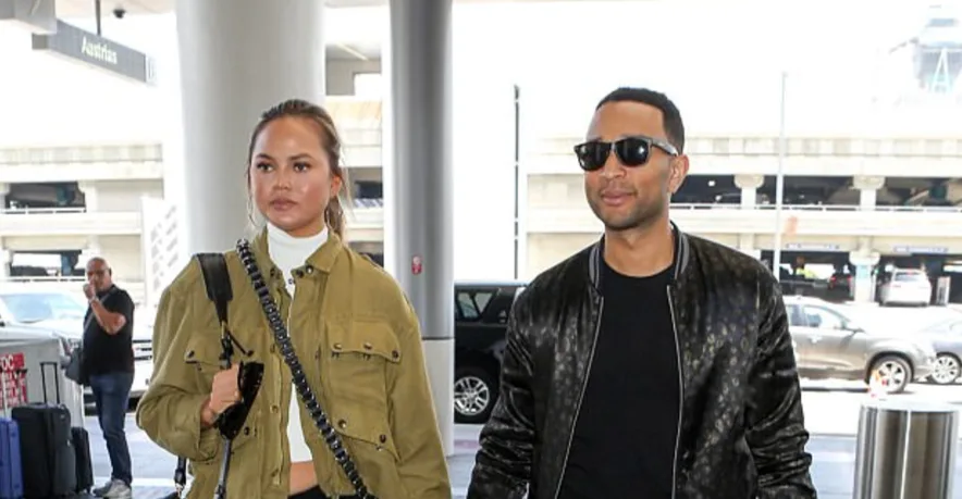 Ο John Legend και η Chrissy Teigen περπατούν σε εξωτερικό χώρο.