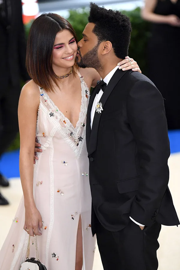 Ο The Weeknd φιλάει τη Selena Gomez στο μάγουλο στο κόκκινο χαλί.
