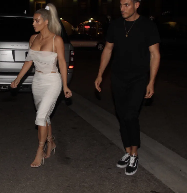 Η Kim Kardashian με λευκό σύνολο περπατά στο δρόμο το βράδυ.