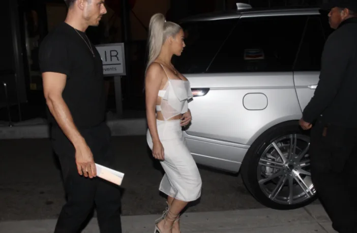 Η Kim Kardashian με λευκό σύνολο δίπλα σε αυτοκίνητο τη νύχτα.