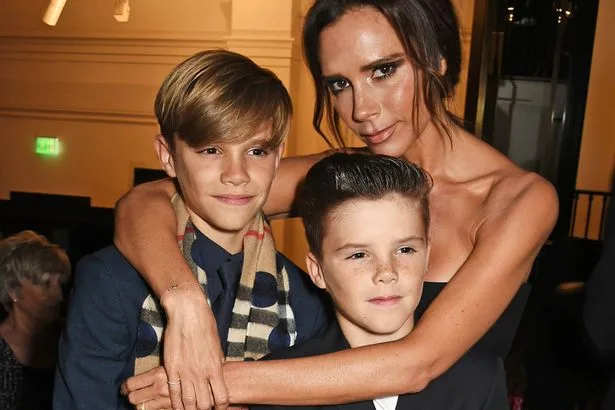 Η Victoria Beckham αγκαλιάζει τους δύο γιους της σε επίσημη εκδήλωση.