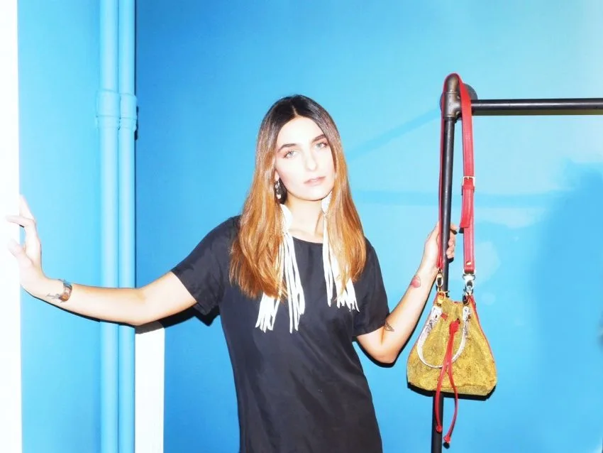 Μία από τις παίκτριες του My Style Rocks, με εντυπωσιακό αξεσουάρ, ποζάρει με αυτοπεποίθηση μπροστά σε μπλε φόντο.