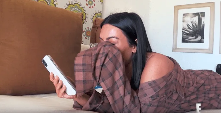 Η Kim Kardashian ξαπλωμένη σε κρεβάτι κρατώντας το κινητό της και καλύπτοντας το πρόσωπό της.