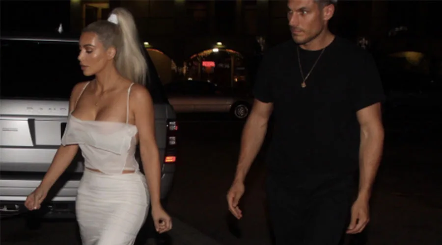 Η Kim Kardashian με λευκό σύνολο και ξανθά μαλλιά δίπλα σε έναν άνδρα.