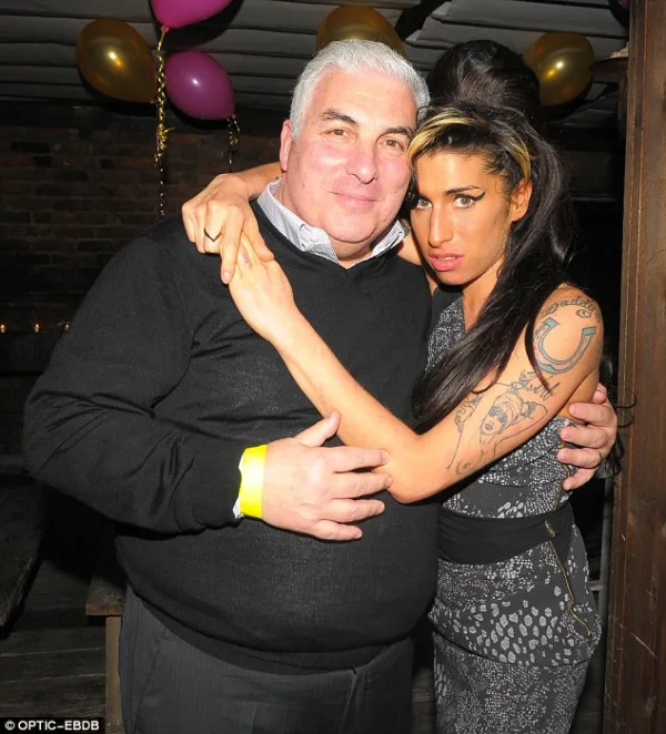 Η Amy Winehouse αγκαλιά με έναν άνδρα σε εσωτερικό χώρο με μπαλόνια.