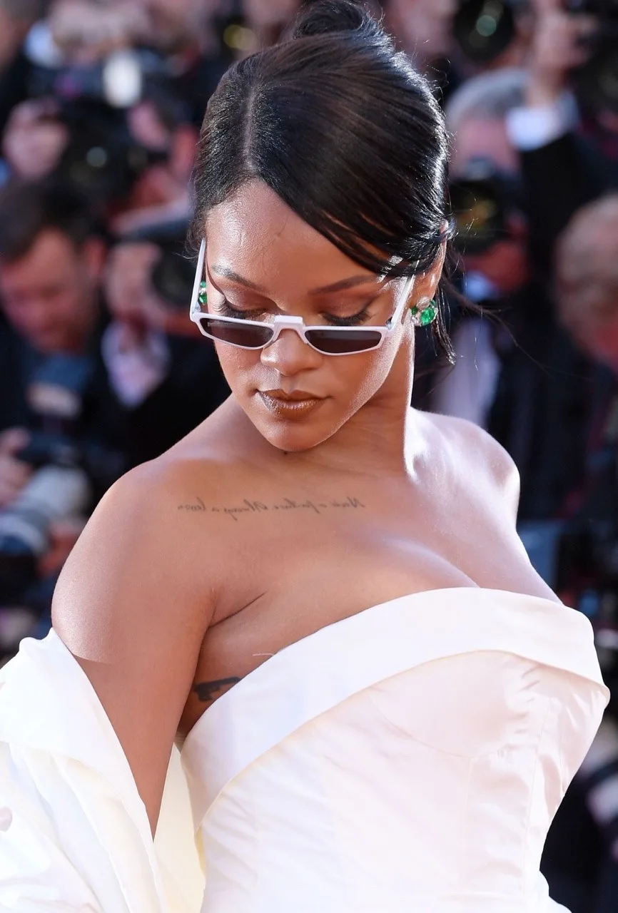 Η Rihanna με λευκό φόρεμα και μικροσκοπικά γυαλιά ηλίου σε κόκκινο χαλί.
