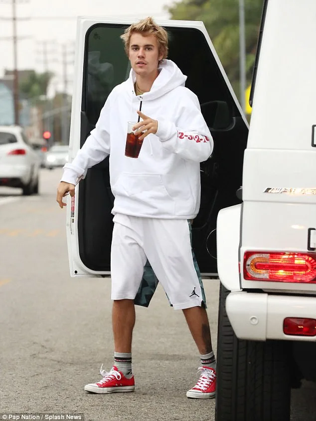 Ο Justin Bieber με λευκό φούτερ και κόκκινα παπούτσια δίπλα σε αυτοκίνητο.