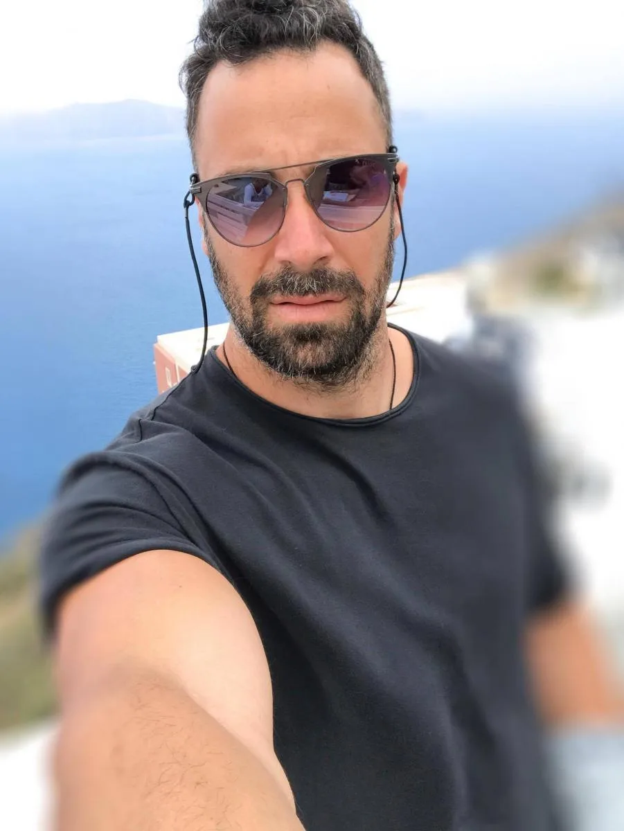 Άνδρας με γυαλιά ηλίου και μαύρο t-shirt σε εξωτερικό χώρο.