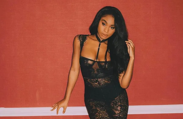 Η Normani Kordei ποζάρει με μαύρο δαντελωτό φόρεμα μπροστά από κόκκινο τοίχο.