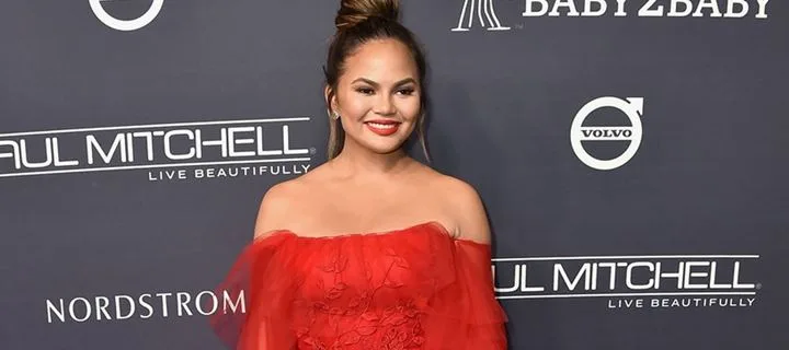 Η Chrissy Teigen με κόκκινο φόρεμα στο κόκκινο χαλί του Baby2Baby Gala.