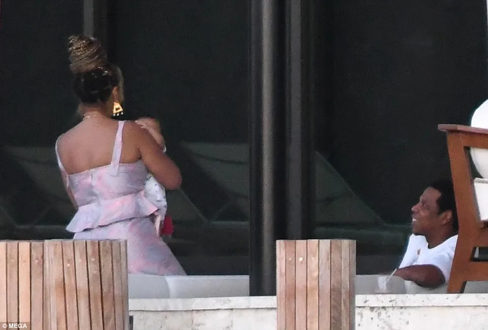 Η Beyoncé κρατάει ένα από τα δίδυμα μωρά της ενώ ο Jay Z την κοιτάζει από απόσταση.