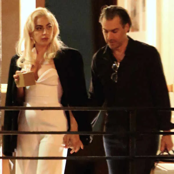 Η Lady Gaga με λευκό σύνολο και μαύρο σακάκι συνοδευόμενη από άνδρα.