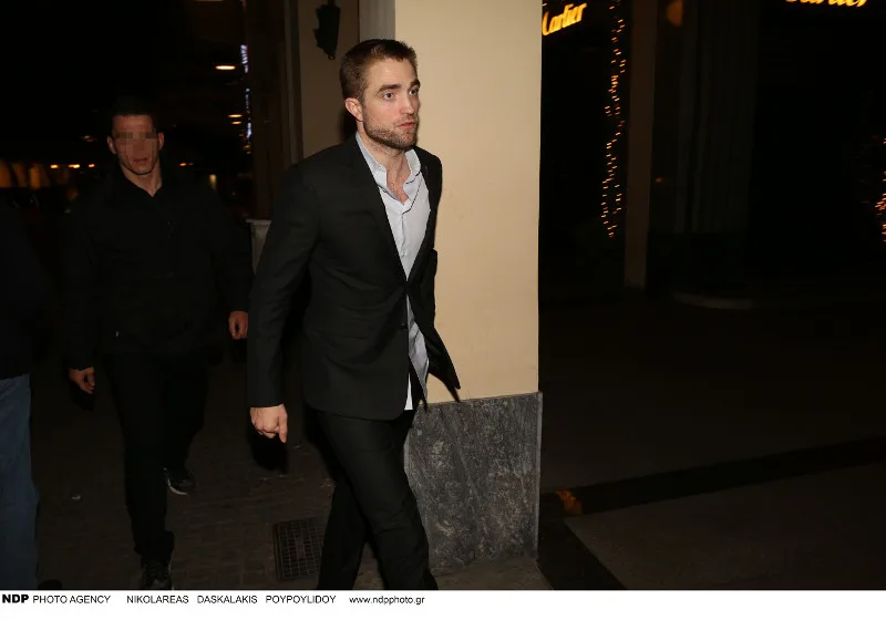 Ο Robert Pattinson περπατάει στο δρόμο το βράδυ φορώντας κοστούμι.