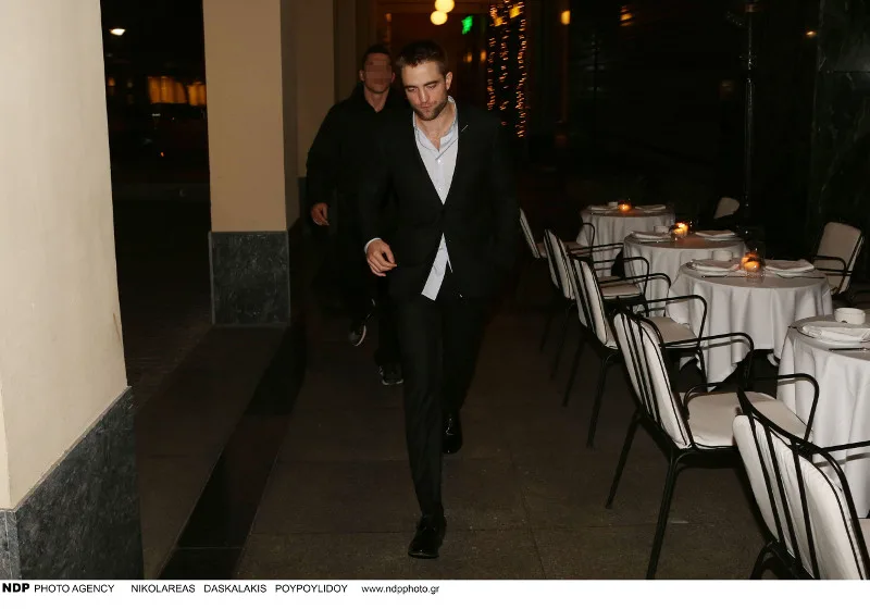 Ο Robert Pattinson περπατά σε εξωτερικό χώρο εστιατορίου στην Αθήνα.