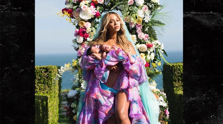 Η Beyoncé κρατάει τα δίδυμα μωρά της μπροστά από μια αψίδα με λουλούδια.