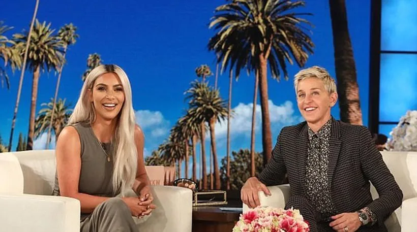 Η Kim Kardashian και η Ellen DeGeneres σε τηλεοπτικό πλατό με φόντο φοίνικες.