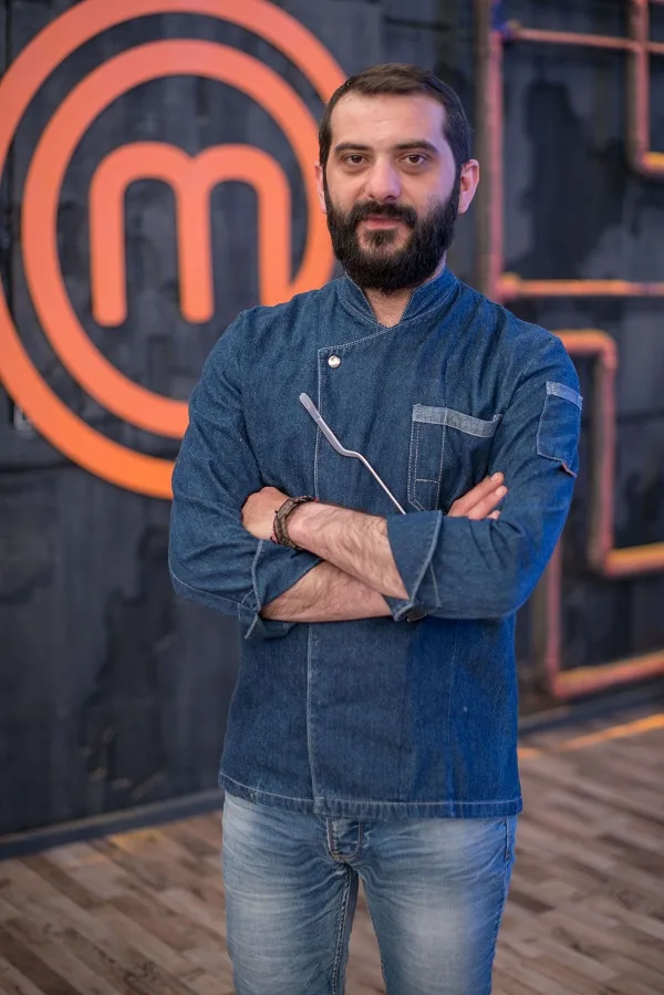 Ο σεφ Λεωνίδας Κουτσόπουλος ποζάρει μπροστά από το λογότυπο του MasterChef.