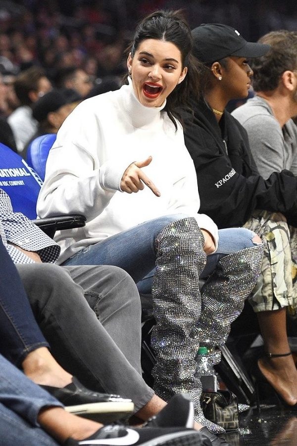 Η Kendall Jenner με λευκό ζιβάγκο και αστραφτερές μπότες σε αγώνα μπάσκετ.