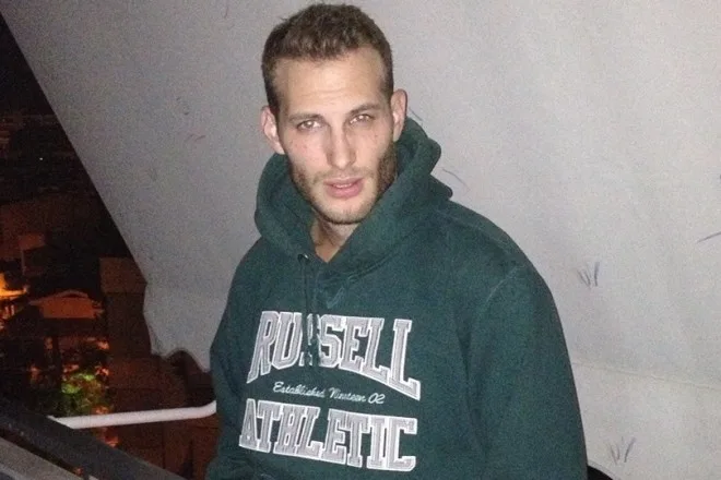 Άνδρας με πράσινο φούτερ Russell Athletic σε εξωτερικό χώρο το βράδυ.