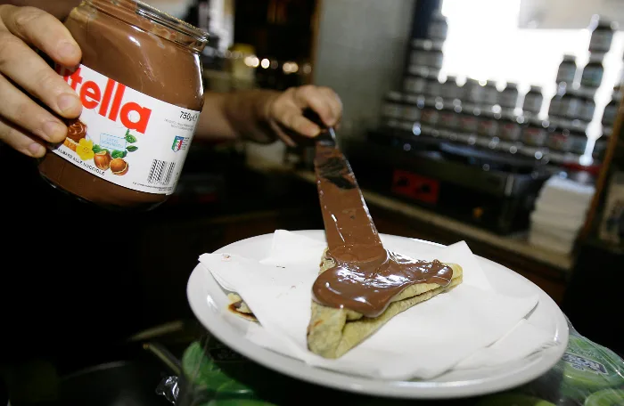 Κοντινό πλάνο σε βάζο Nutella και άλειμμα σοκολάτας πάνω σε κρέπα.