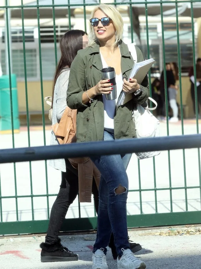Η Κωνσταντίνα Σπυροπούλου με casual look, κρατώντας καφέ και σημειώσεις.