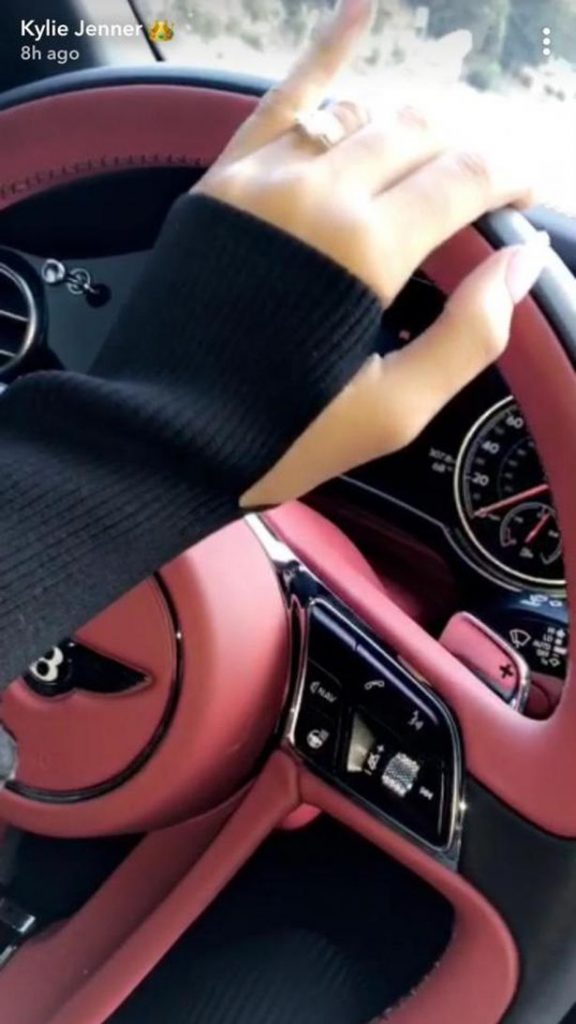 Το χέρι της Kylie Jenner με μονόπετρο στο τιμόνι ενός πολυτελούς αυτοκινήτου.