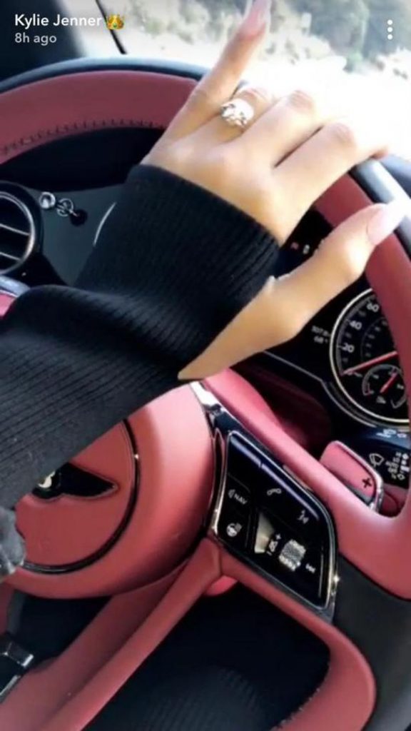 Το χέρι της Kylie Jenner στο τιμόνι ενός πολυτελούς αυτοκινήτου, φορώντας ένα μεγάλο μονόπετρο δαχτυλίδι.