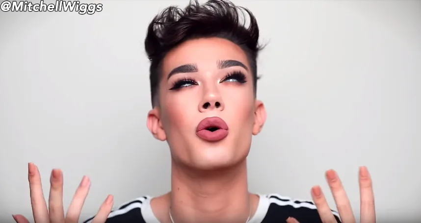 Beauty vlogger με έντονο μακιγιάζ και σηκωμένα χέρια σε λευκό φόντο.