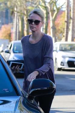 Η Charlize Theron με γυαλιά ηλίου και μωβ μπλούζα δίπλα σε αυτοκίνητο.