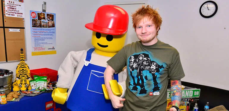 Ο Ed Sheeran ποζάρει δίπλα σε μια μεγάλη φιγούρα Lego.