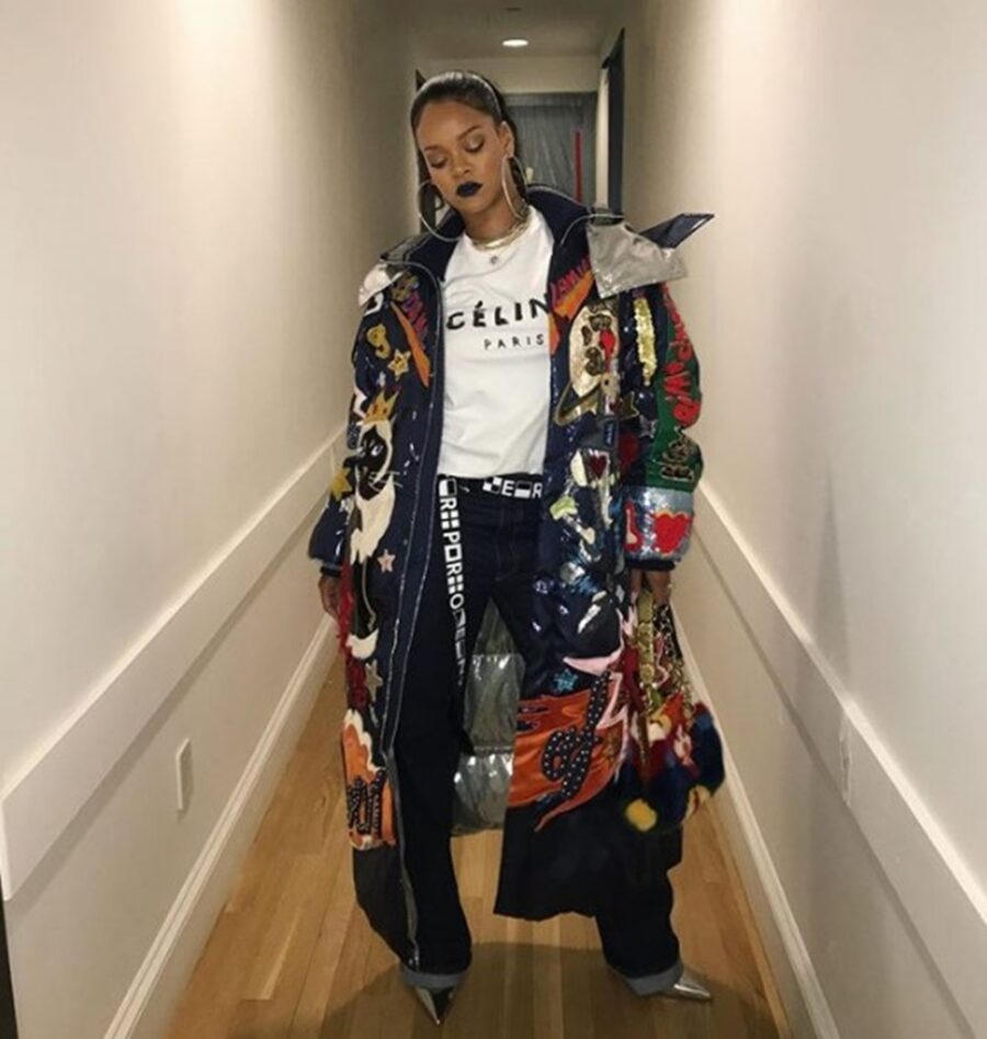 Η Rihanna με πολύχρωμο παλτό και λευκό T-shirt σε διάδρομο.