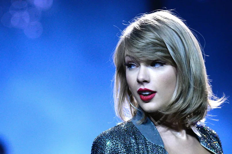 Η Taylor Swift με κοντό ξανθό καρέ και κόκκινο κραγιόν σε σκηνή.