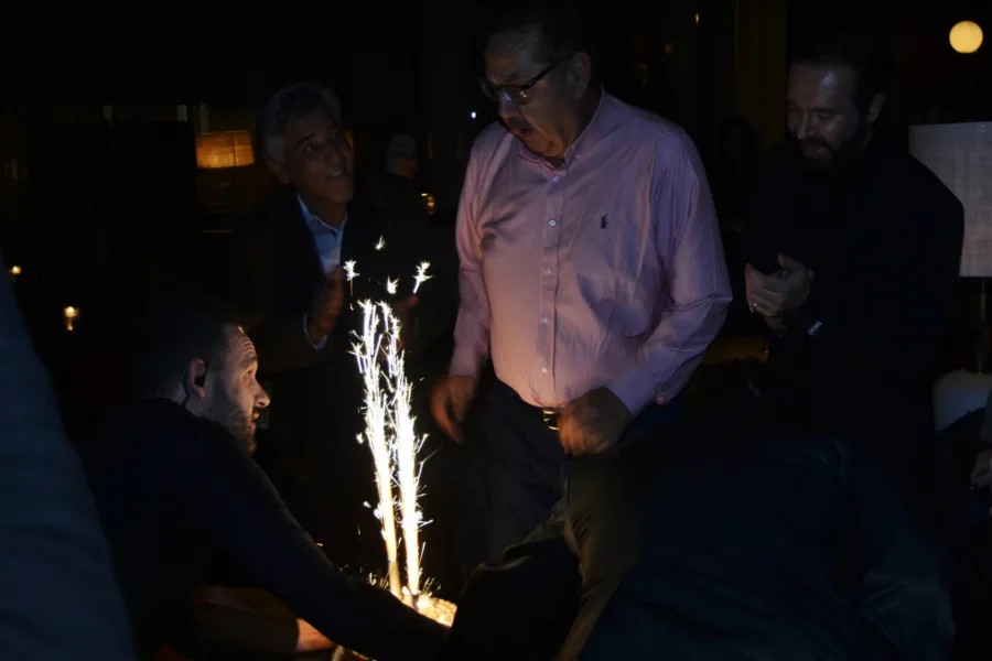 Άνδρες γύρω από μια βασιλόπιτα με αναμμένα πυροτεχνήματα σε σκοτεινό χώρο.
