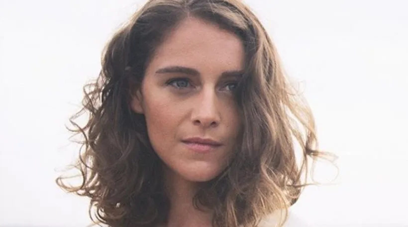 Πορτρέτο της Ariane Labed με κυματιστά μαλλιά σε ανοιχτόχρωμο φόντο.