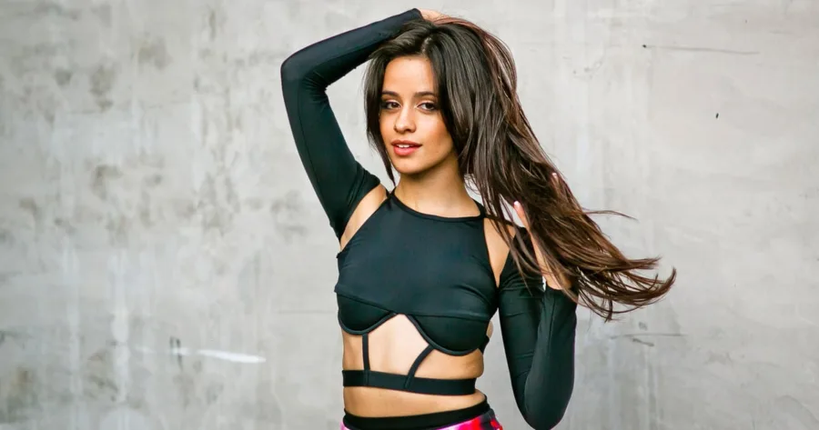 Η Camila Cabello ποζάρει με μαύρο crop top μπροστά από γκρίζο τοίχο.