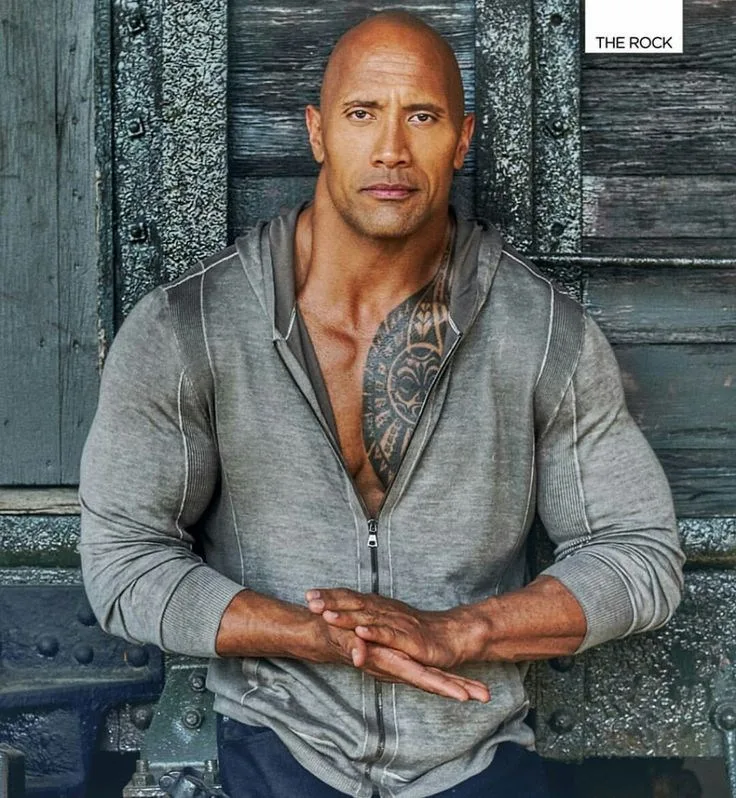 Ο Dwayne Johnson (The Rock) ποζάρει μπροστά από ξύλινη επιφάνεια.