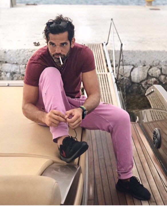 Ο Σταύρος Μαντόπουλος κάθεται σε σκάφος φορώντας μπορντό μπλουζάκι και ροζ παντελόνι.