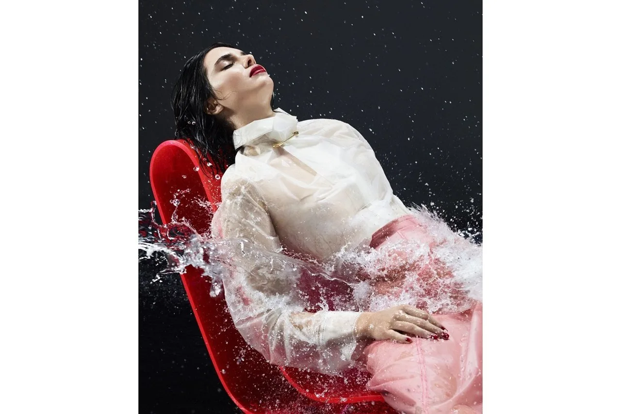 Η Kendall Jenner ποζάρει σε κόκκινο κάθισμα ενώ πέφτει πάνω της νερό.