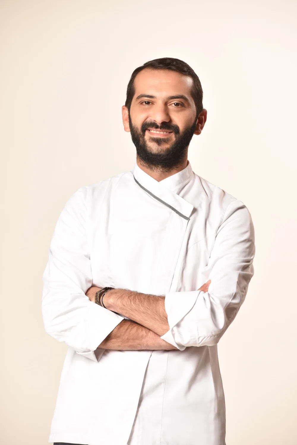 Ο σεφ του MasterChef 2, Σωτήρης Κοντιζάς, με λευκή στολή και σταυρωμένα χέρια, χαμογελάει στον φακό.